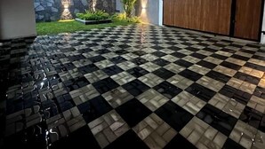 Un espacio al aire libre iluminado de noche, con suelo a cuadros, pared de piedra y valla de madera.