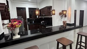 Una cocina moderna con encimera negra, taburetes de madera, lámparas colgantes y un florero con flores.