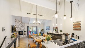 Una cocina moderna con una isla central, un comedor con mobiliario de madera y una sala de estar con chimenea.
