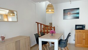 Un coin repas avec une table en bois, des chaises noires, un vase de fleurs, un luminaire suspendu et un four à micro-ondes posé sur un meuble en bois.
