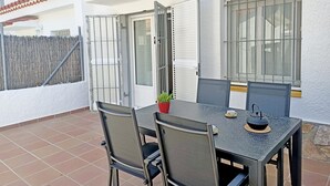 Une terrasse avec une table et des chaises, un pot de fleurs et une fenêtre avec des barreaux.