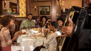 Un groupe de personnes est réuni dans un restaurant dont l’intérieur est décoré de boiseries et dont les murs sont recouverts d’un papier peint à motifs floraux.