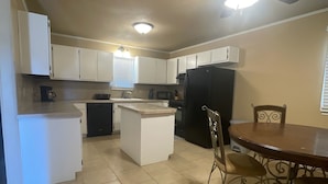 A compact kitchen with white cabinets, a black refrigerator, a ceiling fan, and a dining table with chairs.