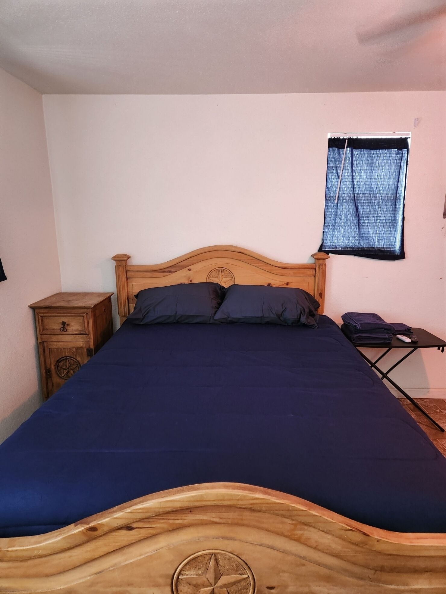 Una cama individual con cabecera de madera, una mesita de noche y una pequeña mesa con un control remoto.