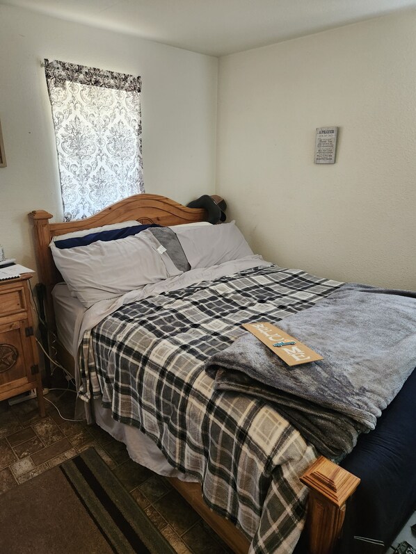 A single-bed room with a wooden headboard, a plaid blanket, and a small bedside table with a lamp.