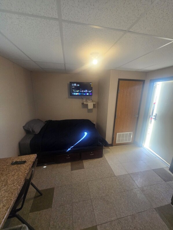 A room with a bed, a TV mounted on the wall, a small table, and a door leading to an outdoor area.