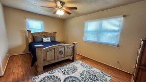 A bedroom with a wooden bed, a ceiling fan, and two windows with blinds.