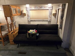 A cozy living room with a dark sofa, wooden side table, and a small table with various items.