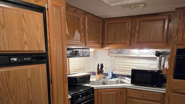 A compact kitchen with wooden cabinets, a built-in oven, a microwave, and a sink.