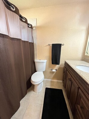 A bathroom with a toilet, a shower curtain, a towel rack, and a sink.