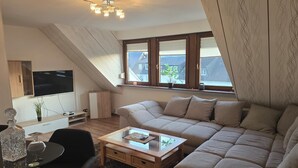 Ein modernes Wohnzimmer mit einer Couch, einem Couchtisch, einem Fernseher und einer Deckenleuchte.
