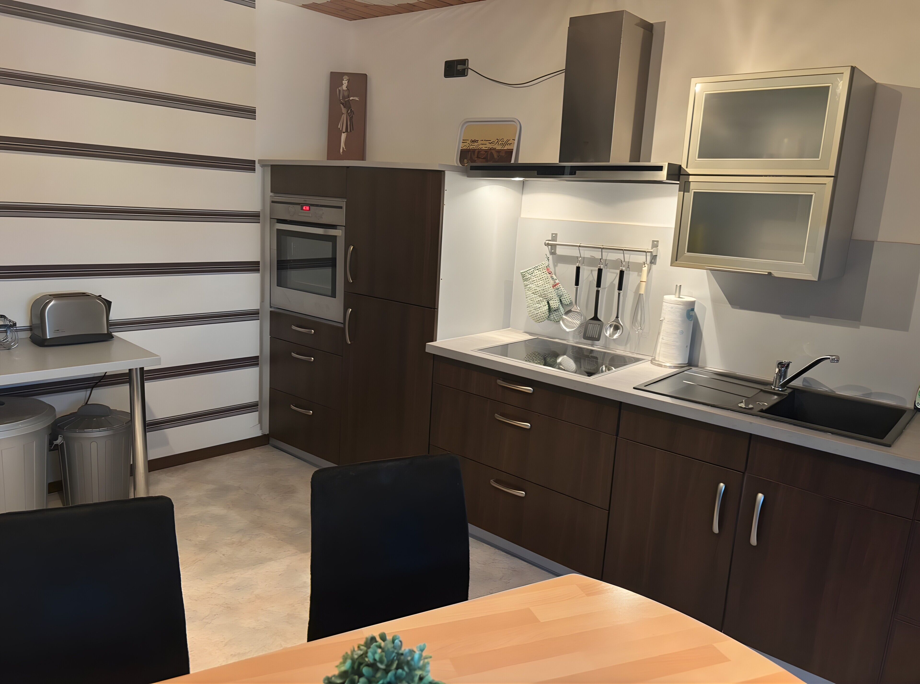 A compact kitchen with a built-in oven, a sink, and a small dining area with a table and chairs.