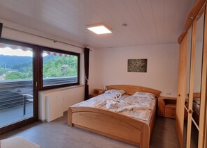 A bedroom with a wooden bed, a window with a view of greenery, a radiator, and a ceiling light. - Apartment 'Haus Erika' with Private Terrace, Shared Garden and Wi-Fi (Bad Teinach-Zavelstein)