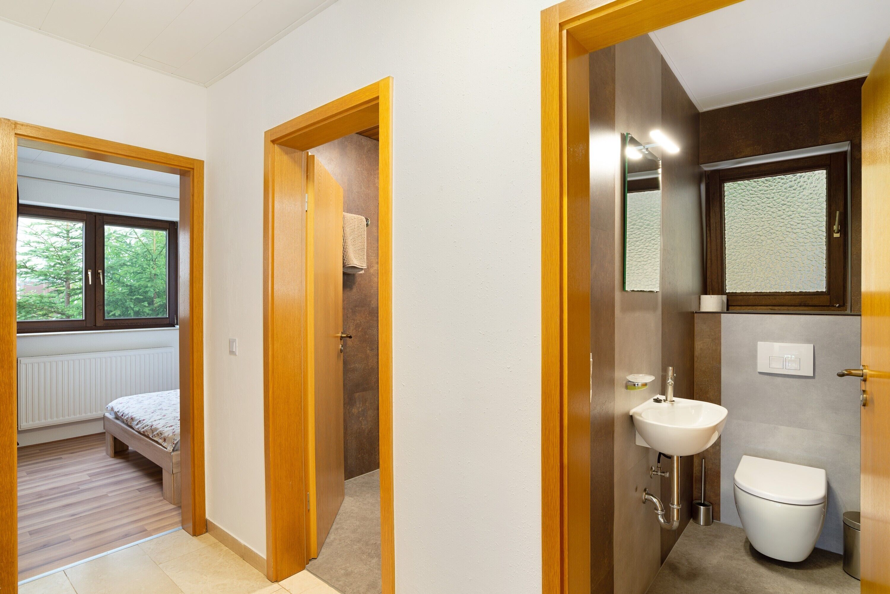 Une chambre avec un lit, une salle de bain avec un lavabo et des toilettes, et un couloir avec une fenêtre.