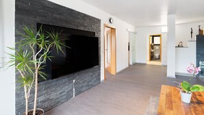 Un soggiorno moderno con un'ampia TV a schermo piatto fissata a una parete in pietra scura, un pavimento in legno e una pianta in vaso su un tavolino in legno.
