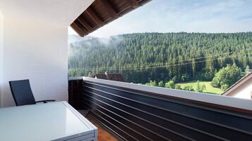 Un balcone con tavolo e sedie, vista su una valle boscosa e una catena montuosa.