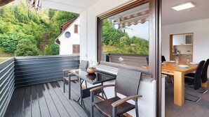 Un balcone con tavolo e sedie, vista su aree verdi e un'area pranzo con tavolo e sedie.