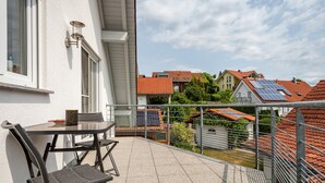 Ein Balkon mit Tisch, Stühlen, Geländer und Blick auf benachbarte Häuser mit Solaranlagen.