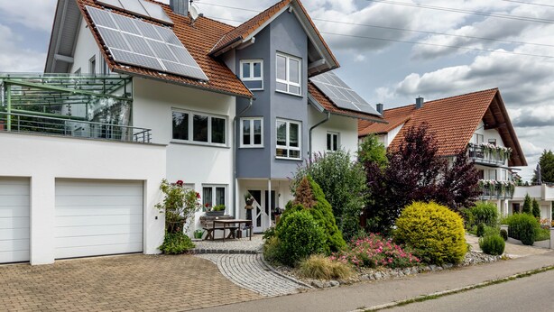 Ein modernes, zweistöckiges Haus mit Solaranlage, einer überdachten Terrasse und einem gepflegten Garten.