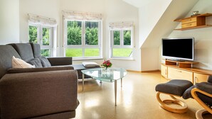 Ein modernes Wohnzimmer mit einer Couch, einem Hocker, einem Glastisch und einem Flachbildfernseher.
