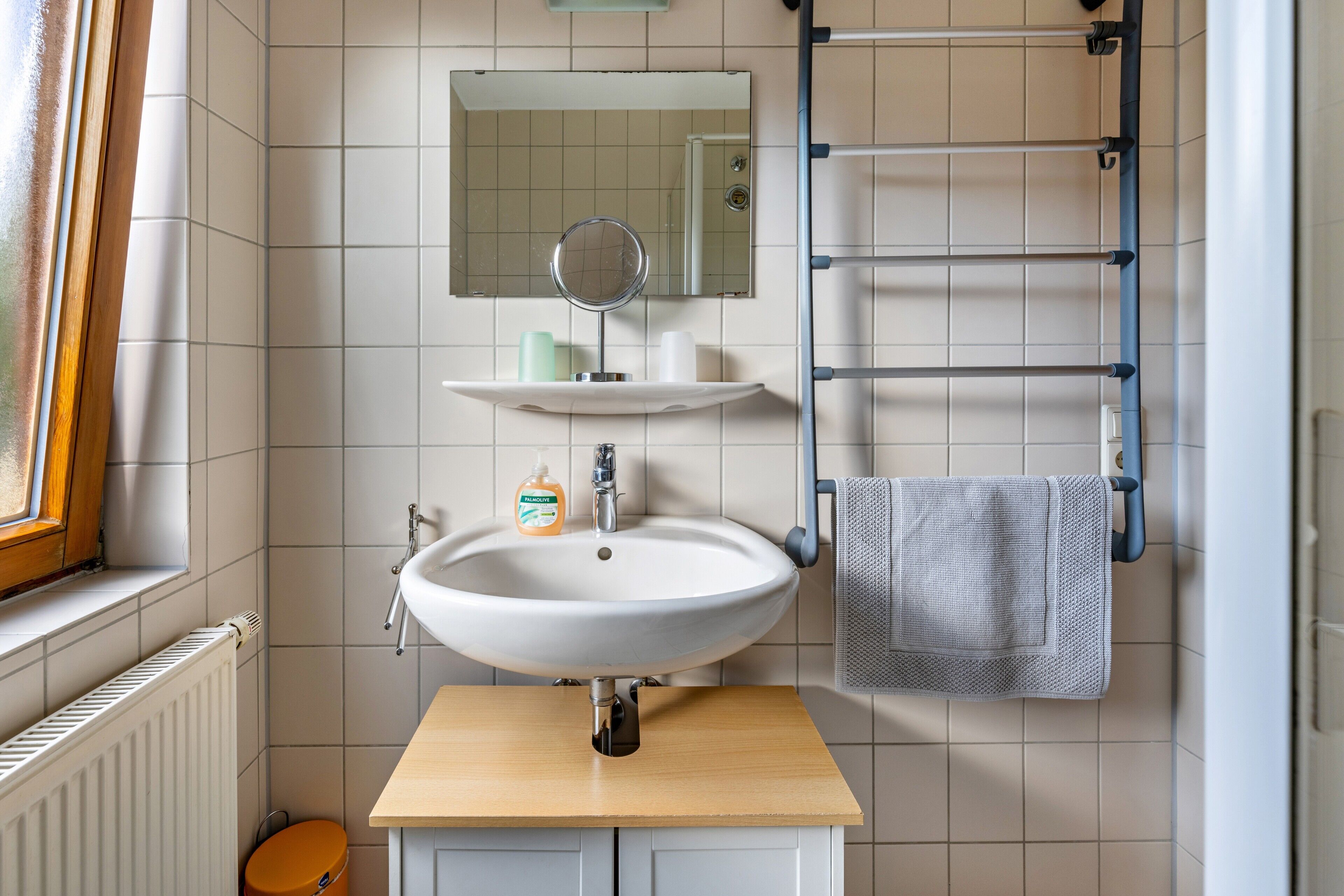 Un baño con lavamanos, espejo, toallero y ventana.