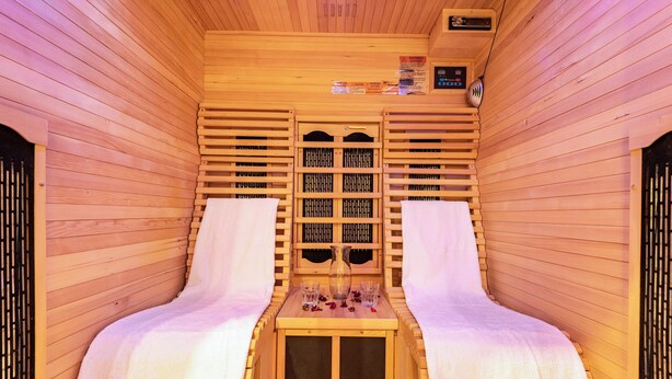 A sauna with wooden walls, two benches, a central table with a vase and glasses, and a control panel.