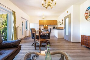 Ein modernes Wohnzimmer mit einer Couch, einem Esstisch mit Stühlen, einer Küchenzeile mit Holzschränken und einer Deckenleuchte.