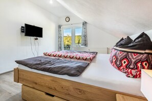 Ein Schlafzimmer mit einem Bett, einem an der Wand montierten Fernseher, einem Fenster mit Vorhängen und einer Heizung.