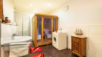 Een badkamer met een glazen douchecabine, een wasmachine, een houten kast en een rood kleed.