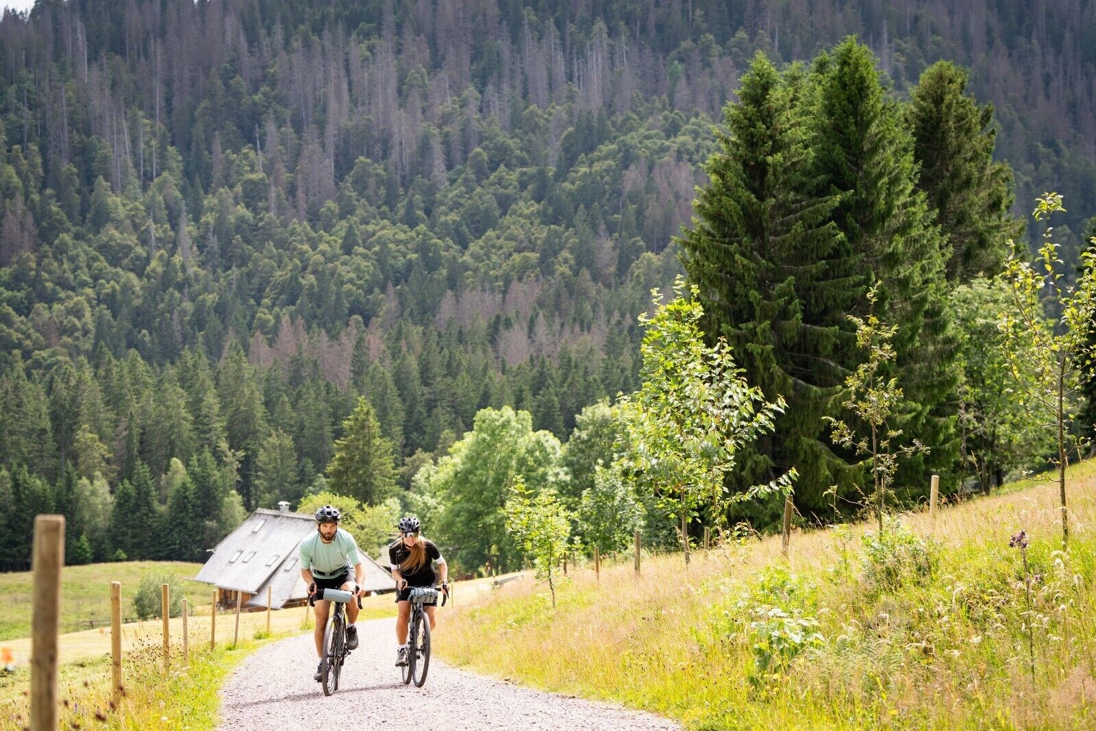 Two cyclists on a gravel path with a forested mountain backdrop.