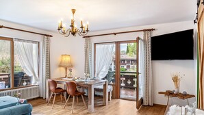 Una habitación con una mesa de comedor, sillas, una araña, un televisor y vistas al exterior.