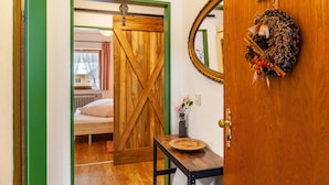 Una habitación con puerta de madera, un espejo, un cartel en la pared y una pequeña mesa con un plato.