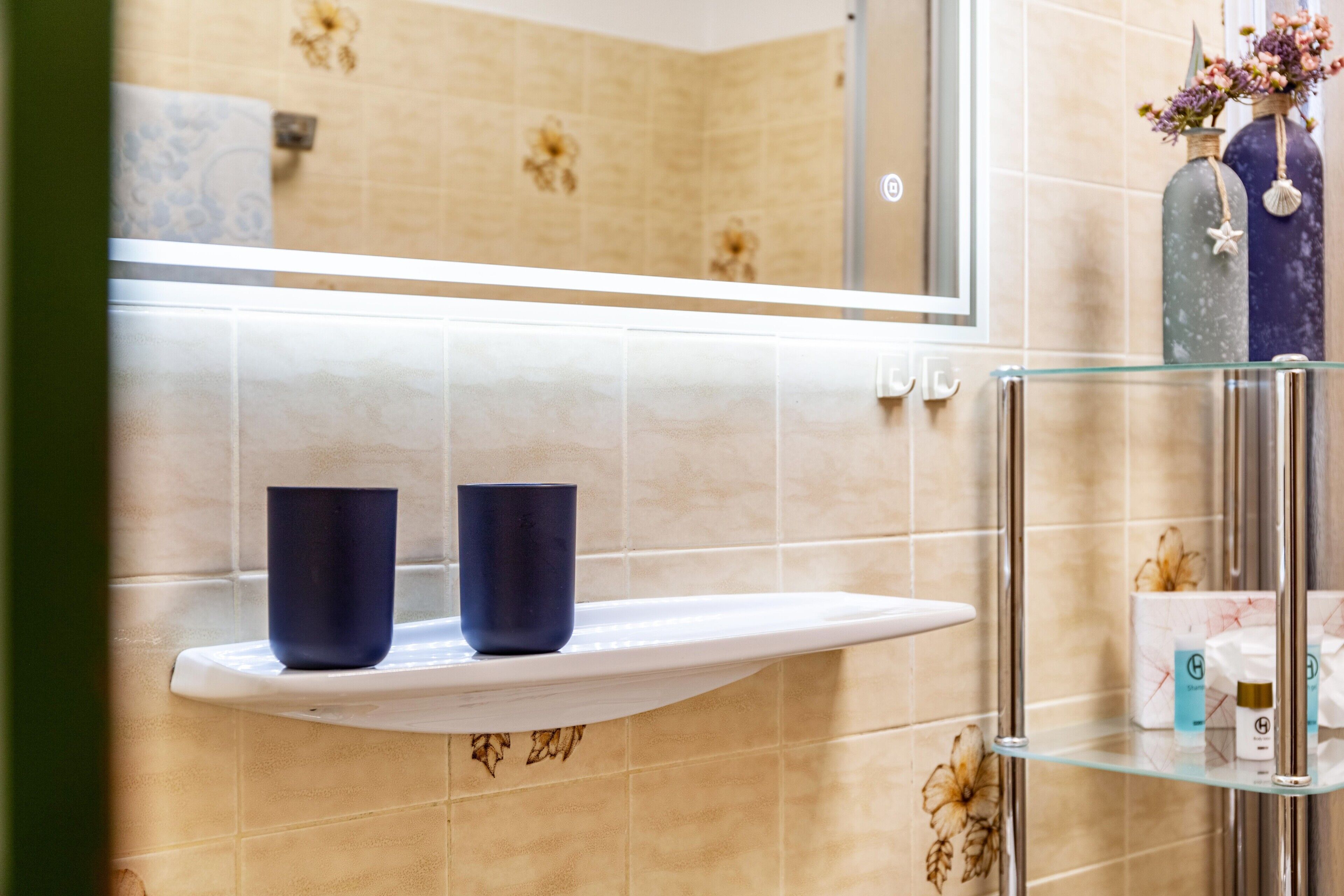 A bathroom with a glass shelf, a mirror, and a tiled wall.