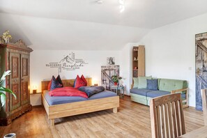 A bedroom with a wooden bed, a green sofa, a wooden cabinet, and a wall with a mountain and text.