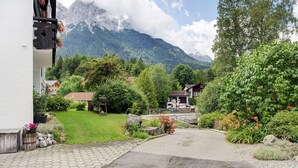 A paved driveway leading to a building with a mountain backdrop. - Studio Apartment 'Aschaubichl - Anemone' with Mountain View, Balcony and Wi-Fi (Grainau)