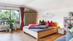 A bedroom with a wooden bed, a view of greenery outside, a radiator, and a wall with text and a mountain illustration. - Studio Apartment 'Aschaubichl - Anemone' with Mountain View, Balcony and Wi-Fi (Grainau)