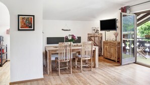 A dining area with a wooden table and chairs, a television, and a glass door leading to an outdoor area. - Studio Apartment 'Aschaubichl - Anemone' with Mountain View, Balcony and Wi-Fi (Grainau)