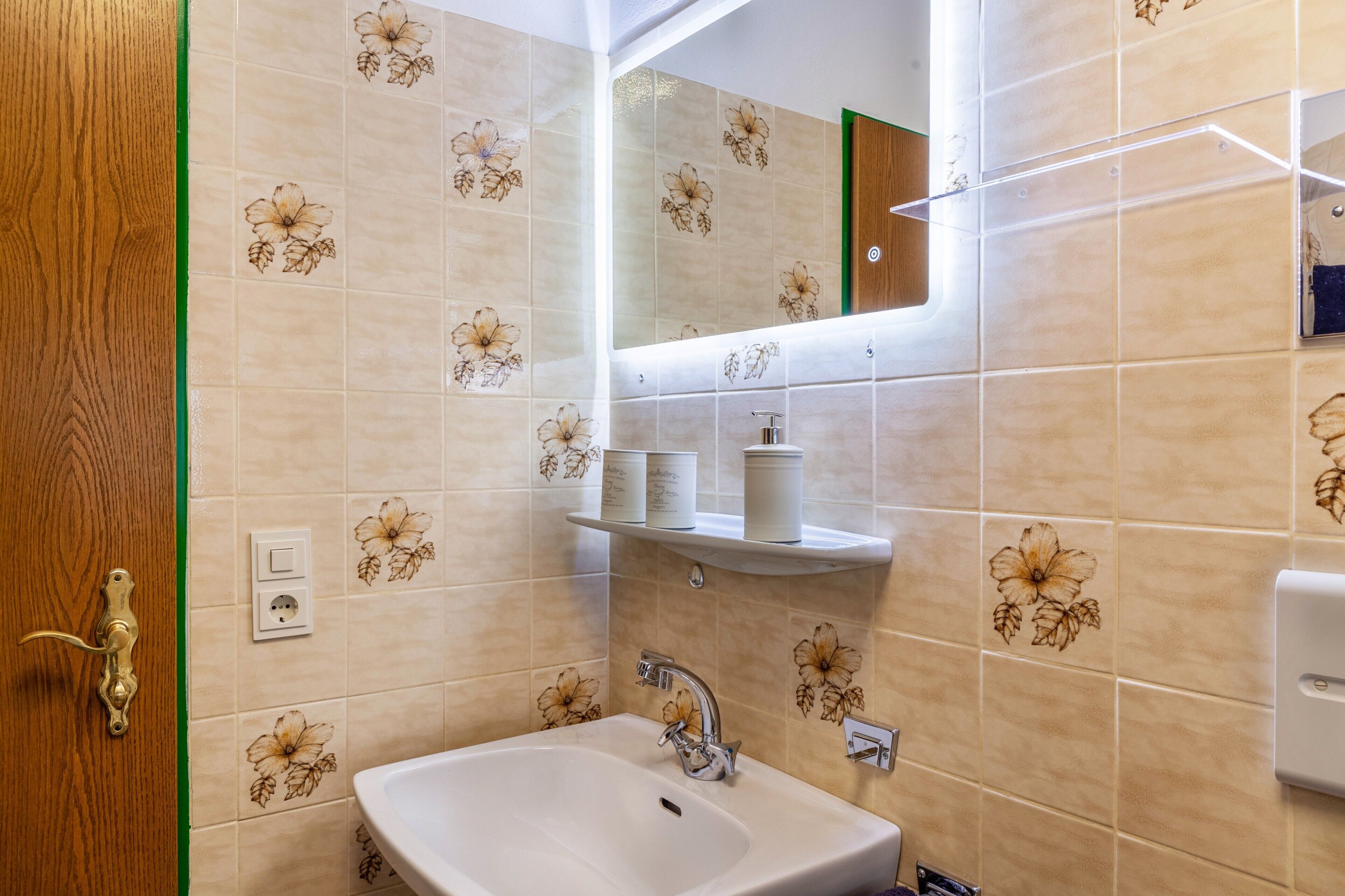 Een badkamer met bloementegels, een wastafel, een spiegel en een plank met toiletartikelen.