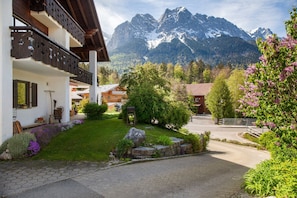 A mountain lodge with a stone pathway, wooden balconies, and a view of snow-capped mountains.
