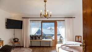 Ein Schlafzimmer mit Bett, Fernseher, Heizkörper, einem Fenster mit Vorhängen und einer Pendelleuchte.