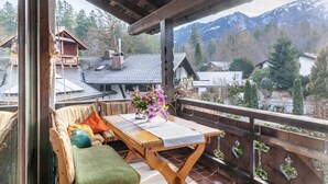 Ein Holzbalkon mit Tisch, Kissen und einem Blumenvasen.