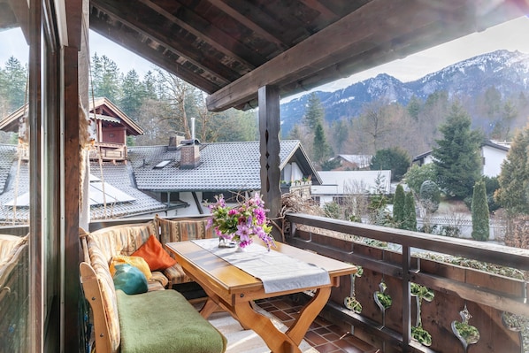 A wooden balcony with a table, cushions, and a vase of flowers.