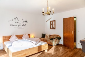 A bedroom with a wooden bed, a sofa, a wooden wardrobe, and a chandelier.