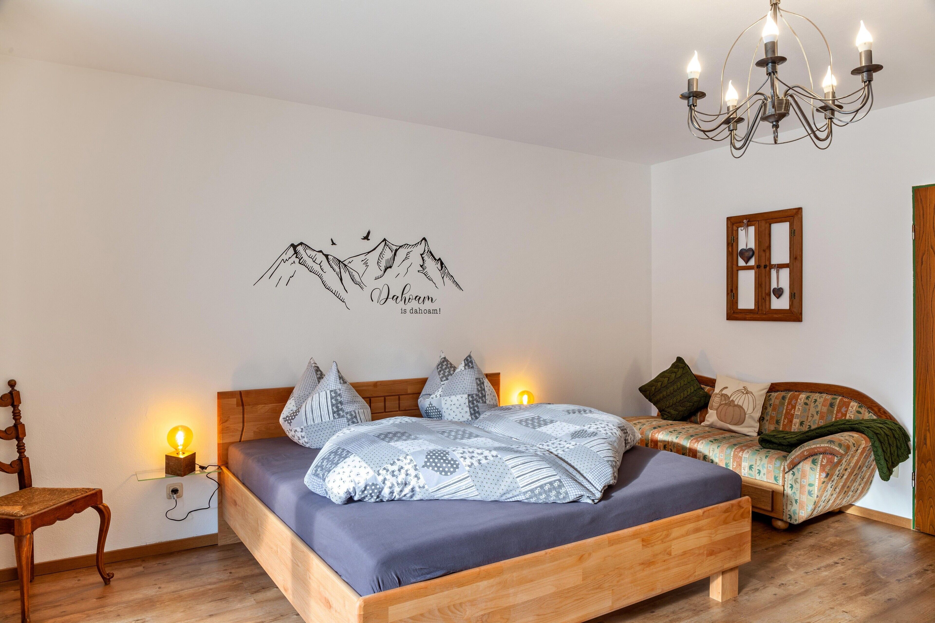 Ein Schlafzimmer mit Bett, Nachttisch, Stuhl, Schlafsofa und einer Deckenleuchte sowie einer Wanddekoration.