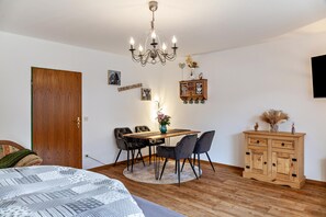 Une pièce comprenant un lit, une table à manger en bois avec des chaises, un lustre, une armoire et un téléviseur fixé au mur.