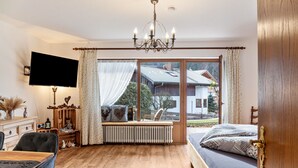 A bedroom with a bed, a desk, a chair, a radiator, a TV, and a large window with curtains.