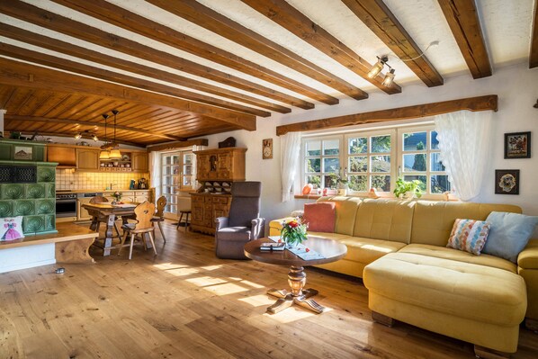 Una sala de estar acogedora con vigas de madera, un sof á, una mesa de comedor y una zona de cocina.