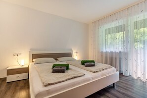 A double bed with two pillows, a nightstand with a lamp, and a window with sheer curtains.