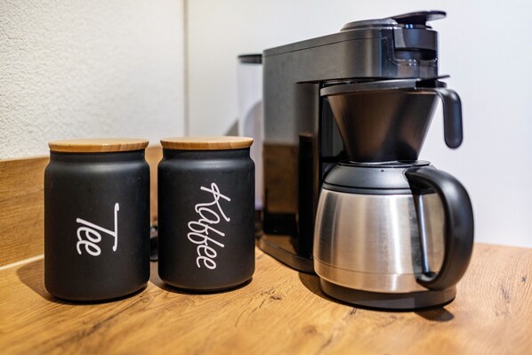 Two black containers with wooden lids and a black coffee maker on a wooden surface.