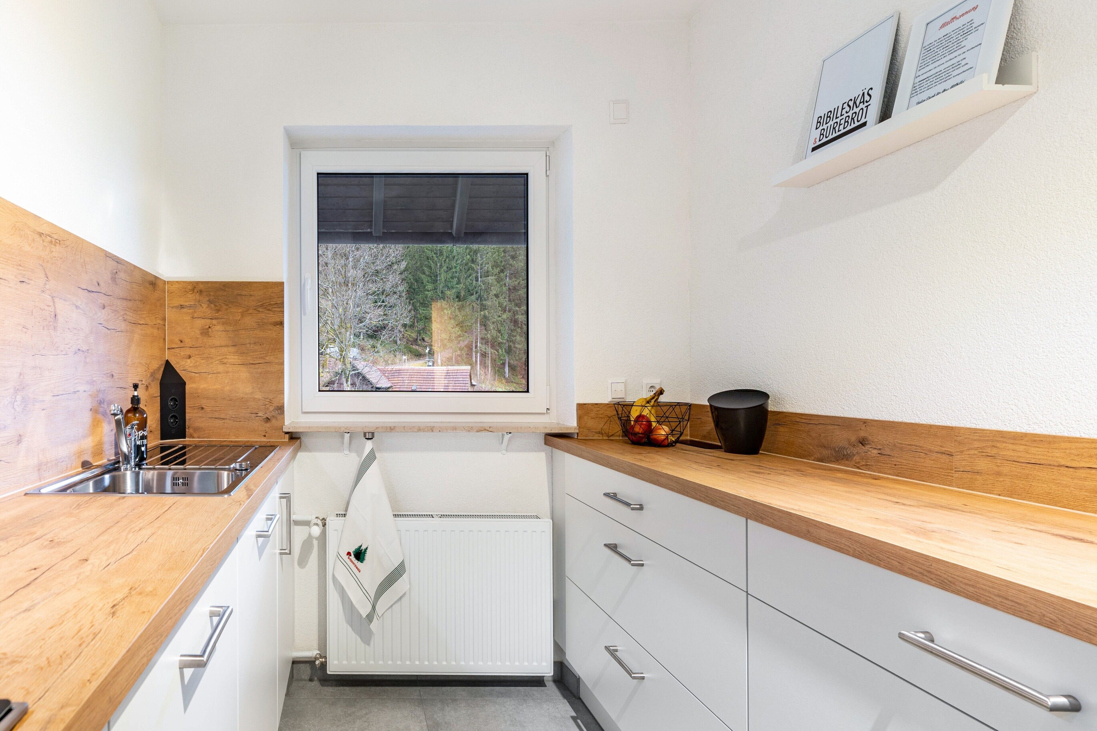 Een moderne keuken met een houten aanrecht, witte kastjes, een raam met uitzicht en een plank met een bord.